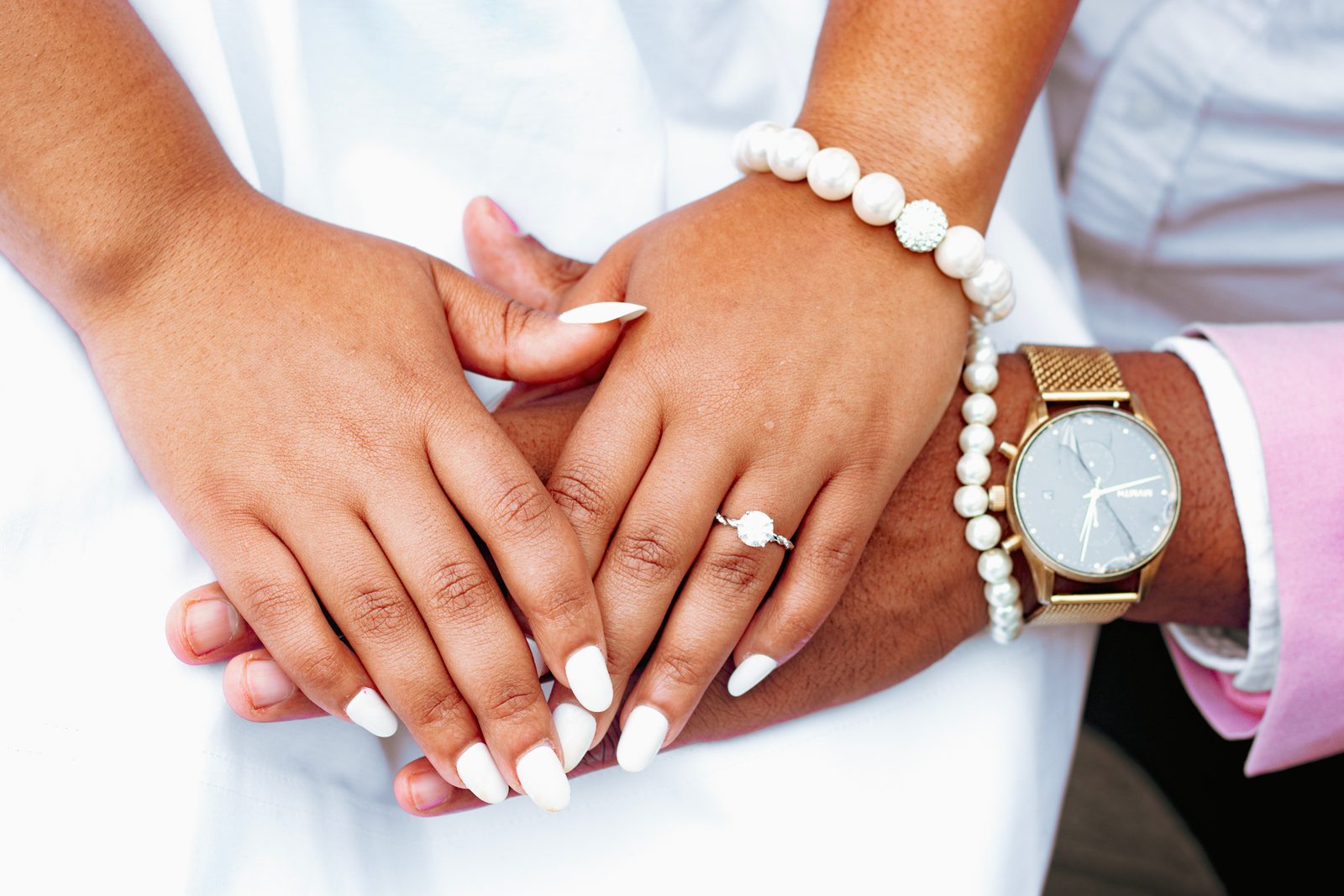 Detail of intertwined hands with engagement ring, pearls, and watch