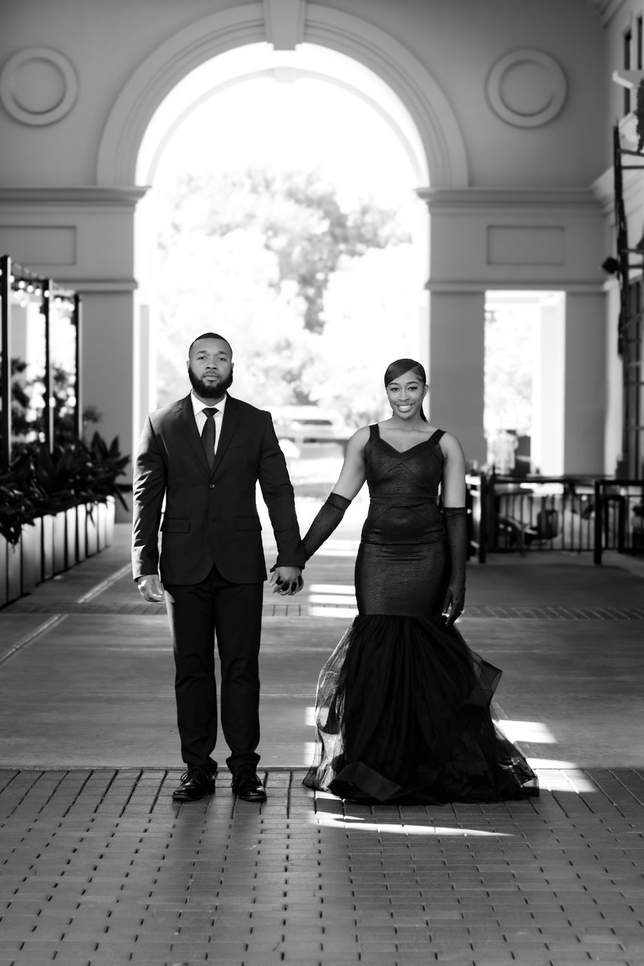 Couple in black formalwear holding hands beneath an archway
