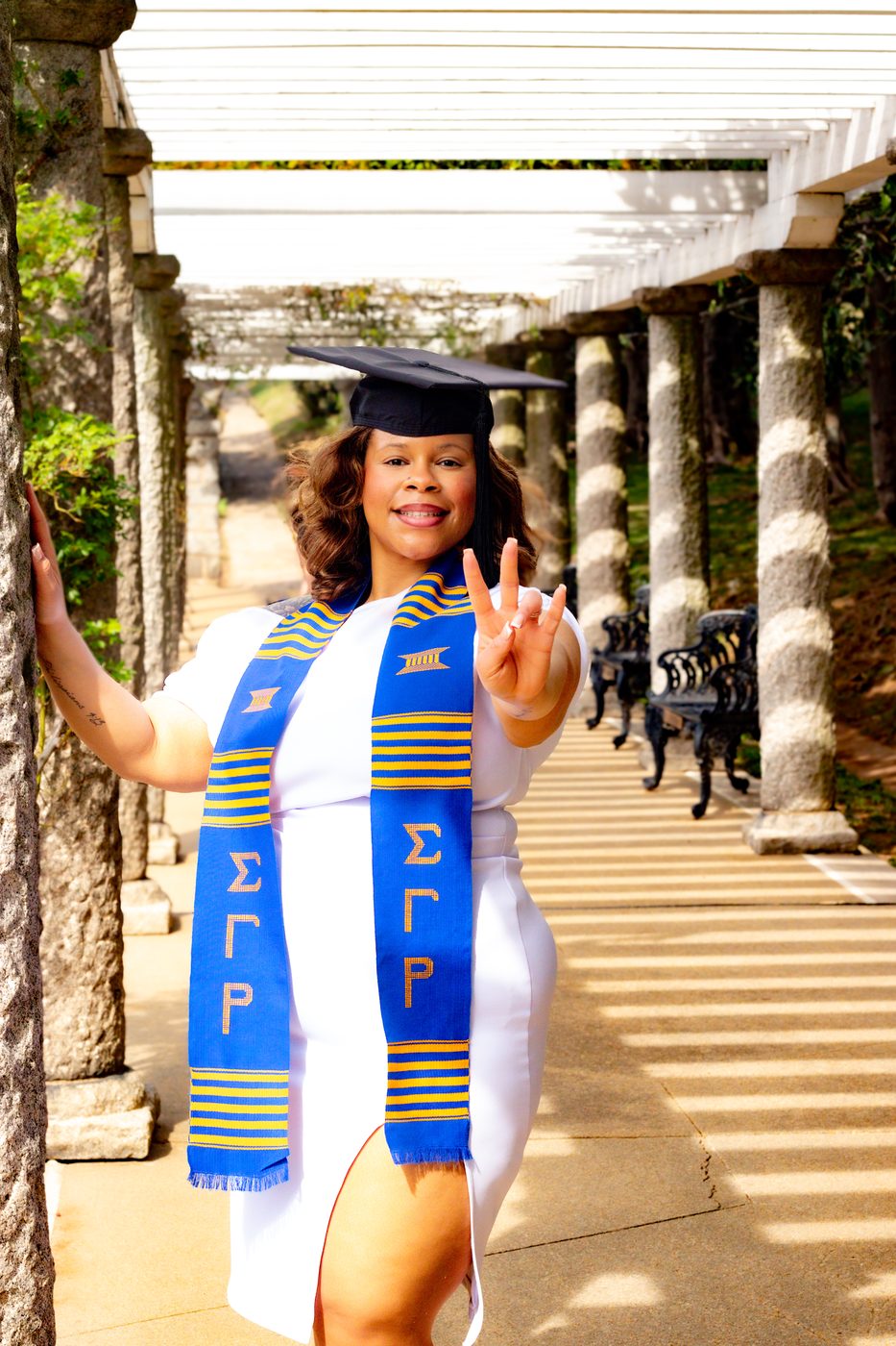 Graduate in cap and sorority stole under a garden colonnade